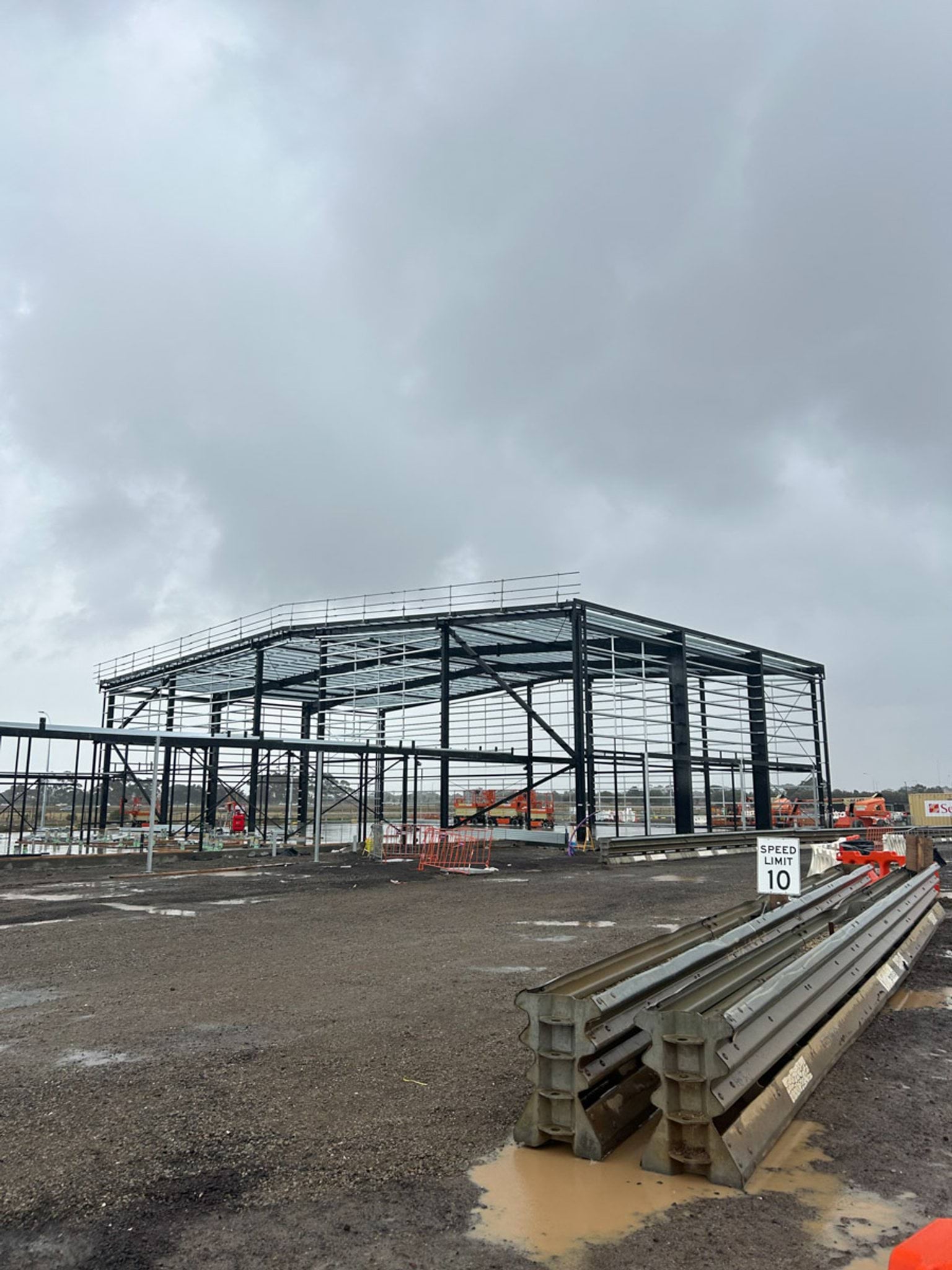 A large steel framework forming part of a school building, with stacked materials and safety signage visible on site.