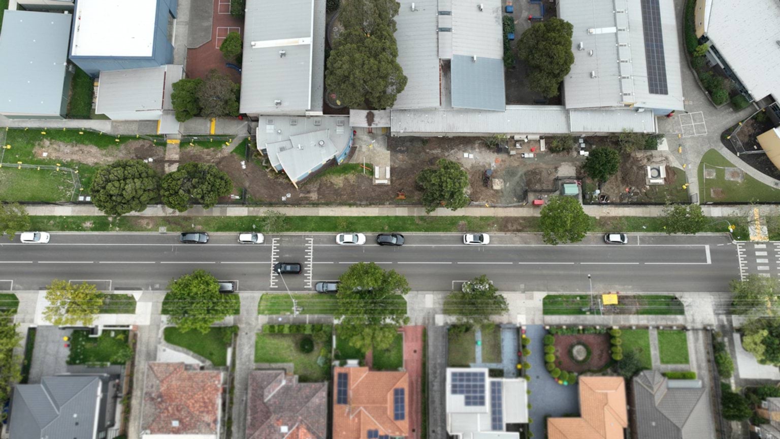 Top‑down aerial image of school buildings and grounds along a residential street, showing construction works between buildings.