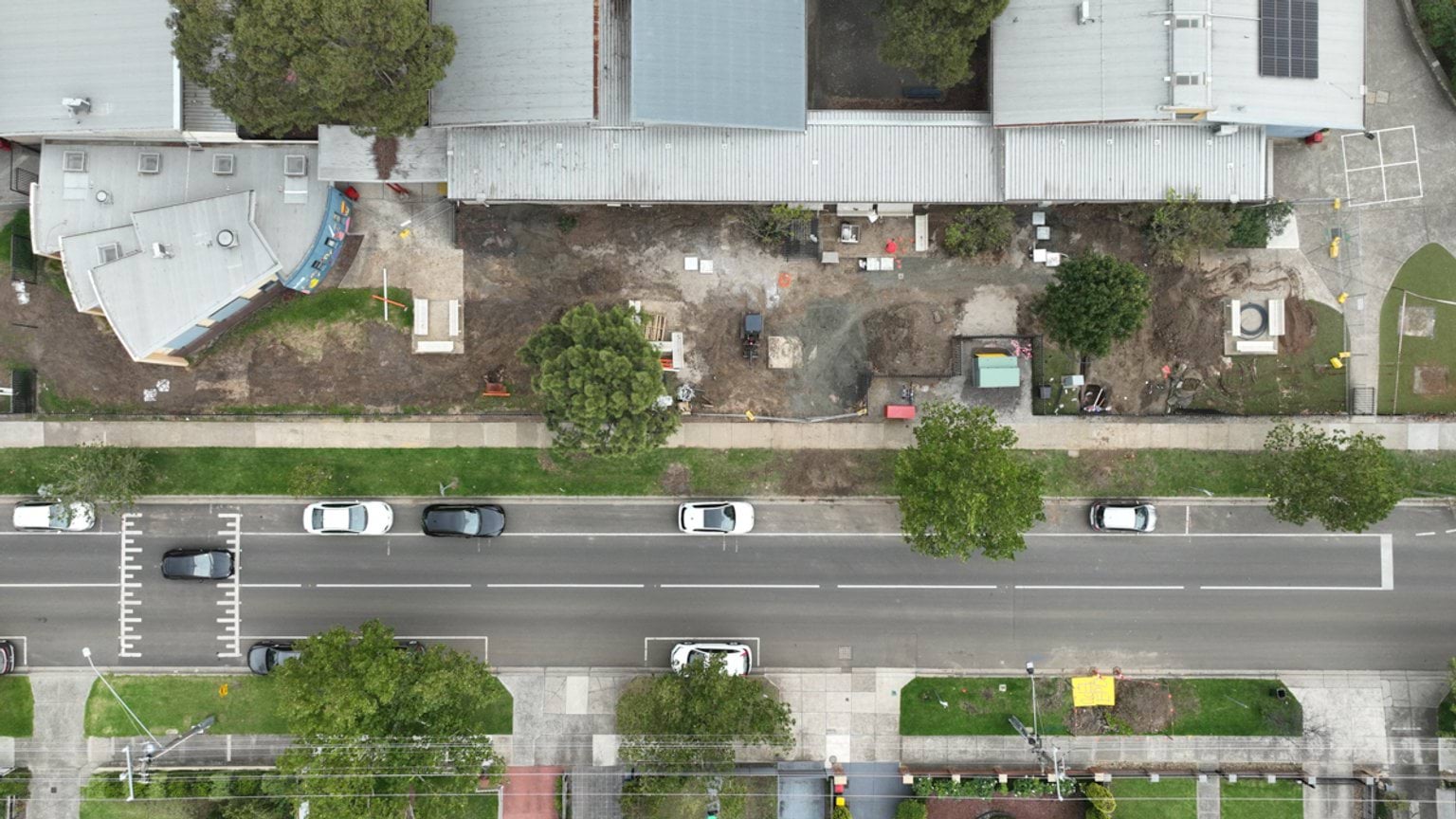 High‑angle aerial view of school buildings with an active construction zone along the street boundary.