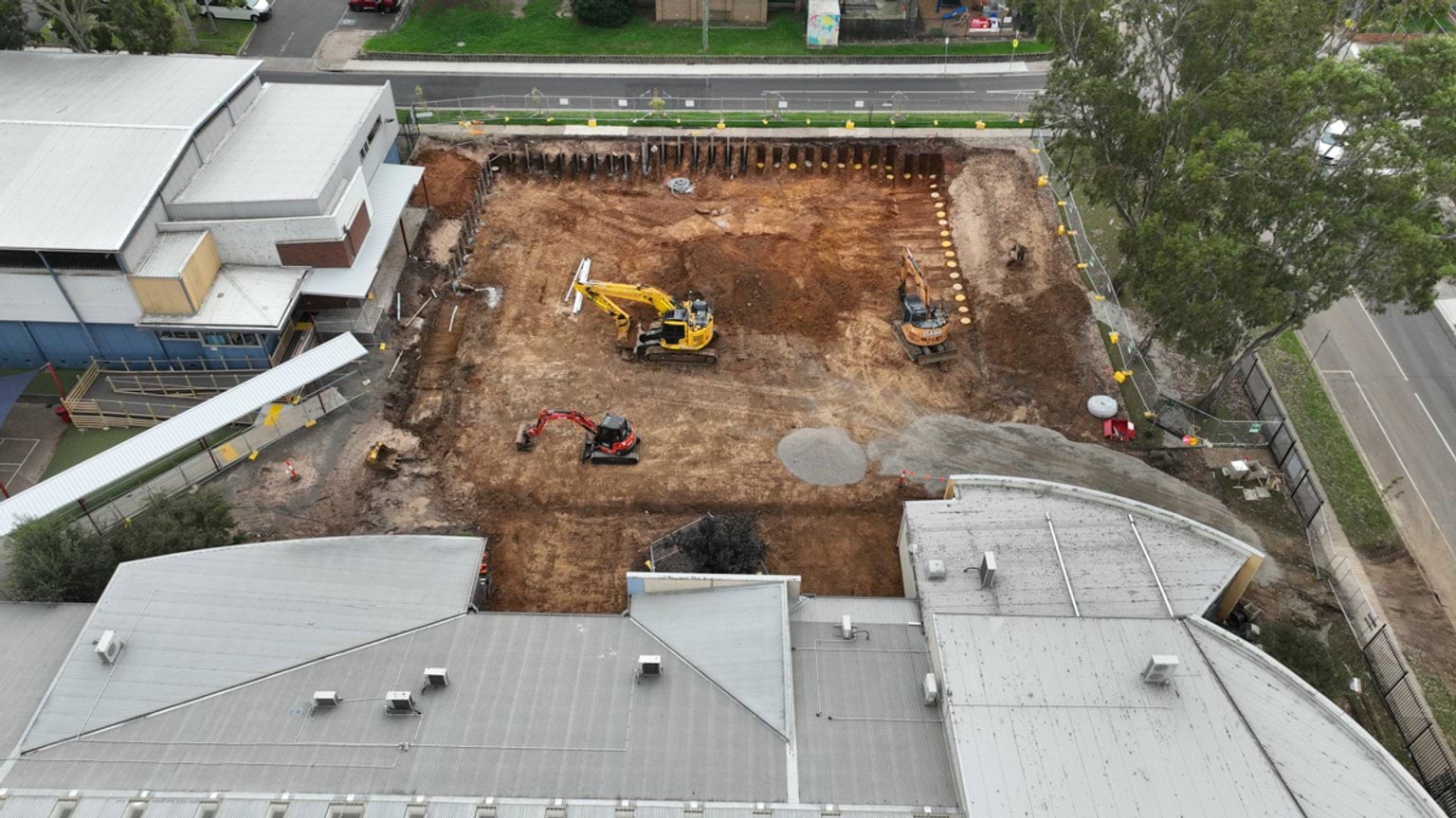 Aerial view of a school courtyard under redevelopment with excavators operating between surrounding buildings.