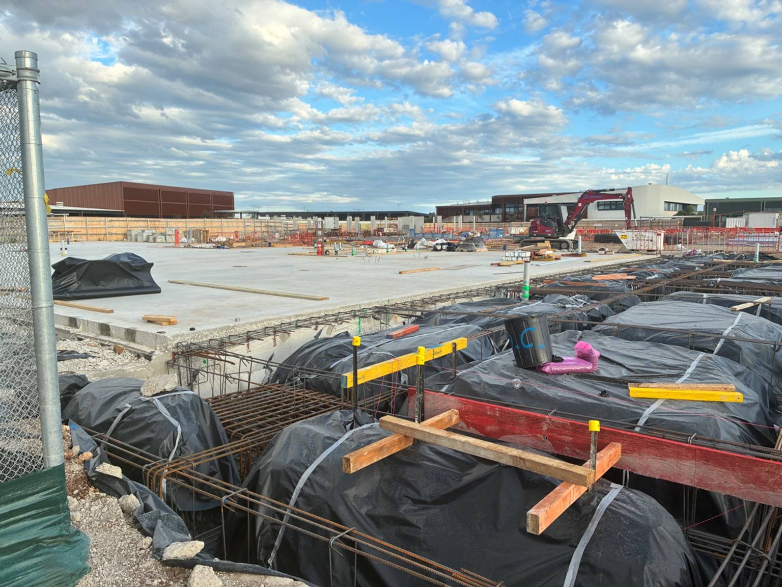Partially completed concrete slab at a school construction site, with exposed footings and construction machinery nearby.