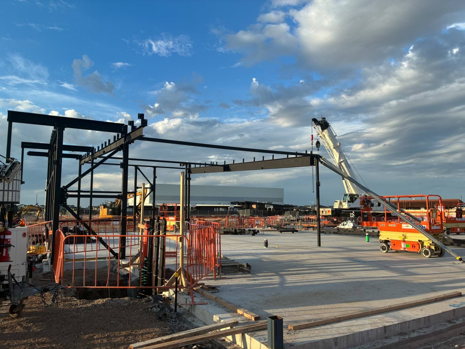 Steel structural framing being erected on a newly poured concrete slab at a school construction site.