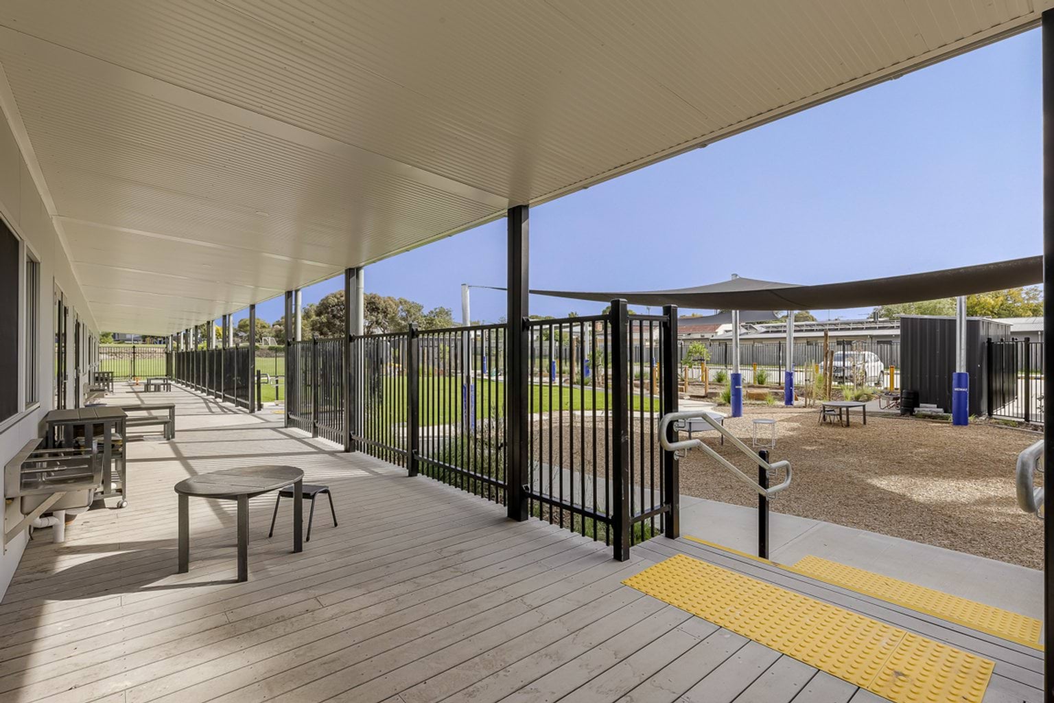 Covered outdoor walkway with seating, accessible ramp and fenced transition to the school playground.