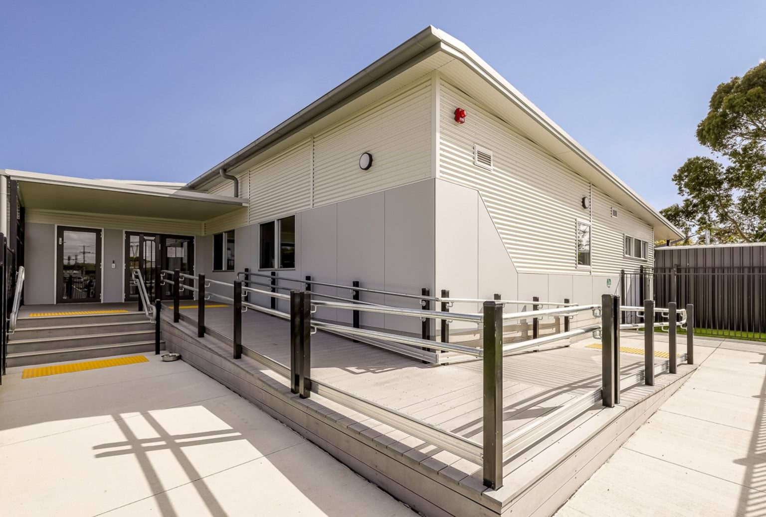 Accessible school entrance showing ramps, handrails and steps leading to a modern classroom building.