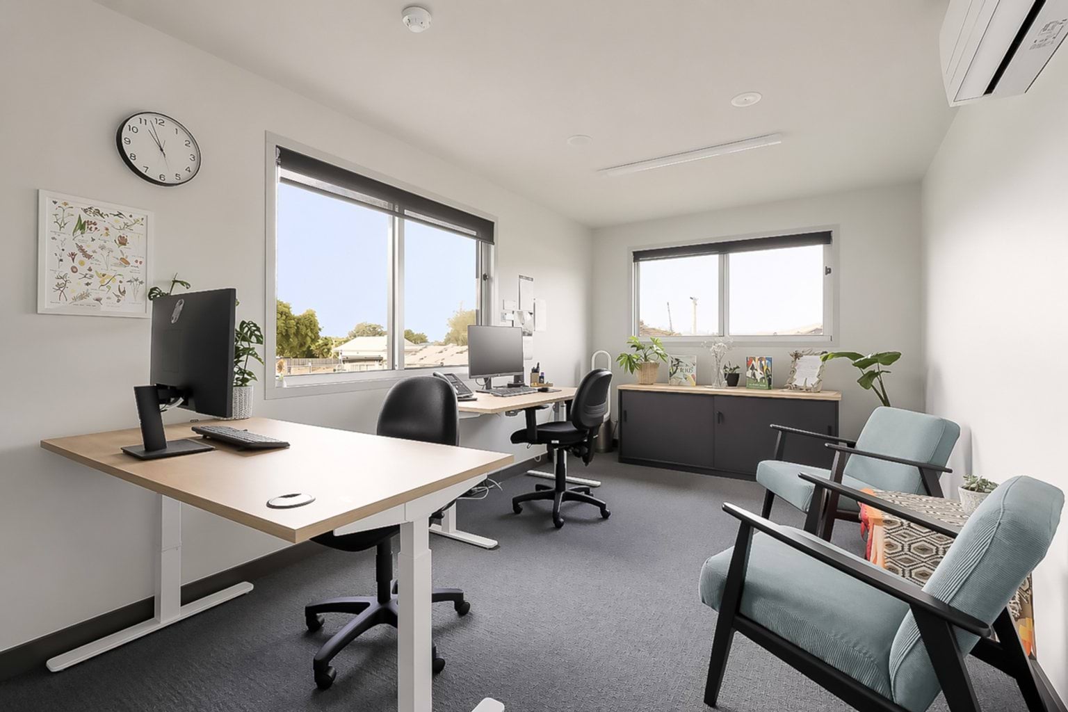 Staff office with desks, computers, storage cabinets and seating beside large windows.