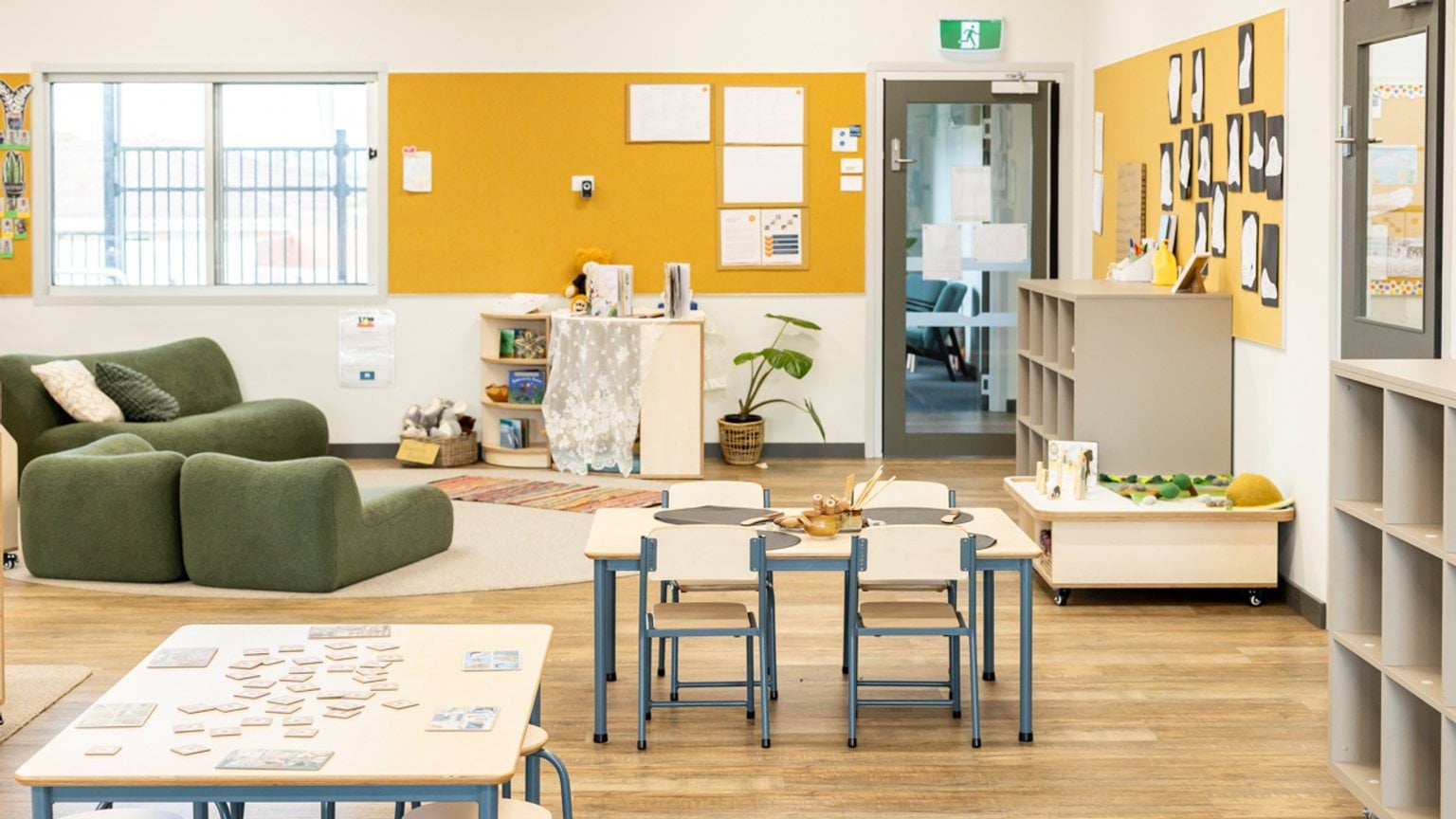Early learning classroom with child‑sized tables, soft seating, open shelving and display boards.