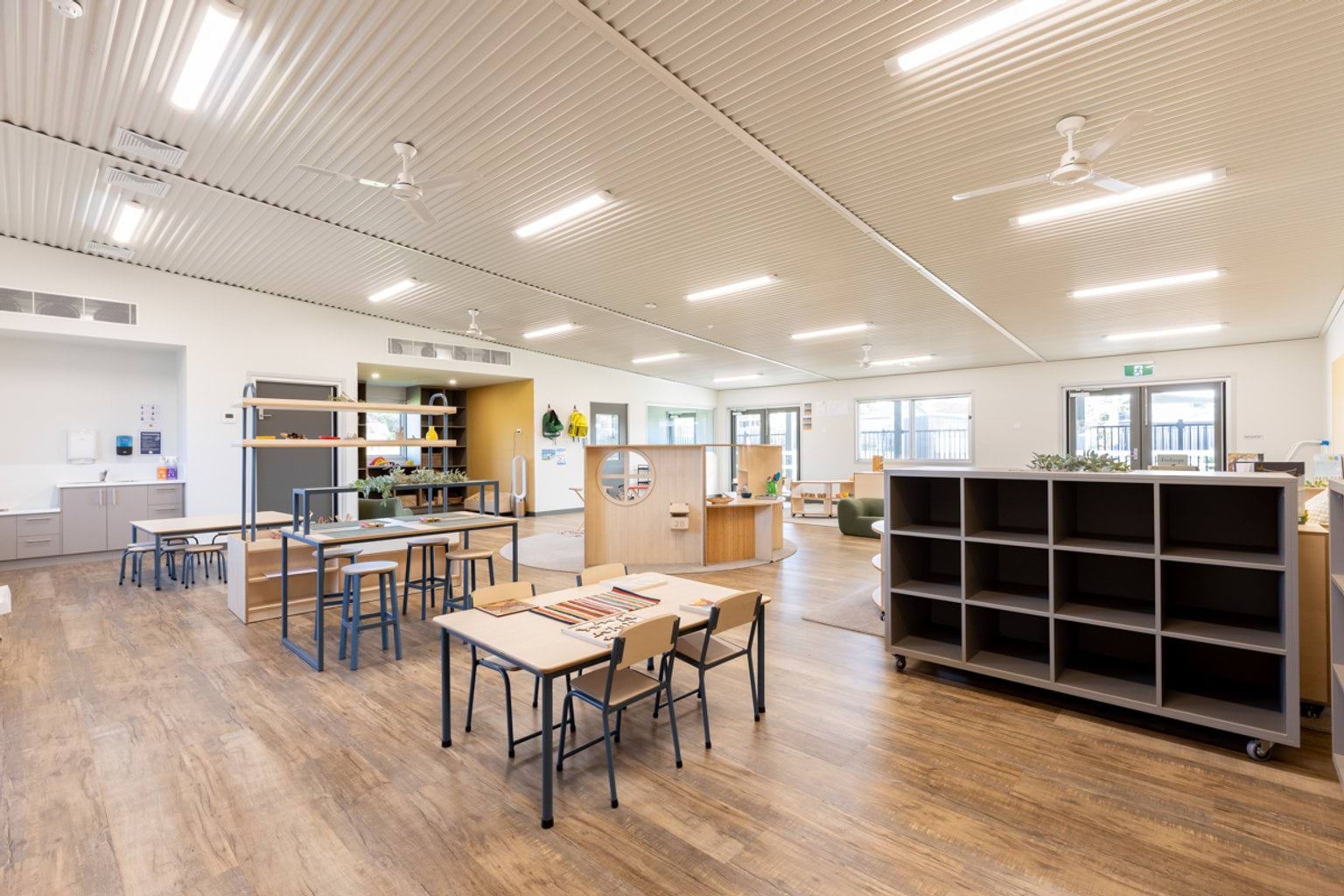 Bright early learning classroom with child‑sized tables, open shelving, learning zones and natural light.