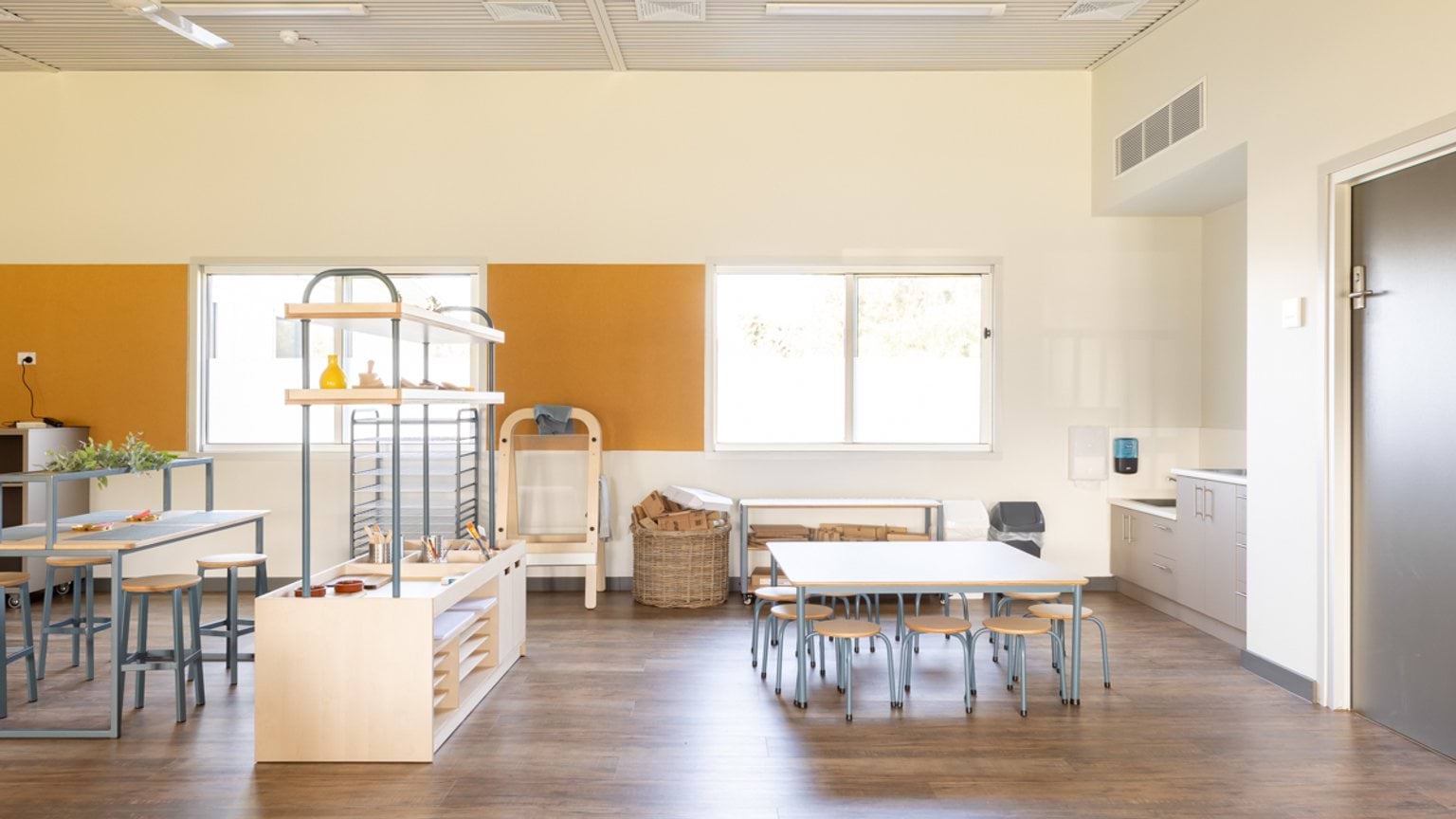 Early childhood classroom showing a craft and play area with low tables, storage units and sink facilities.