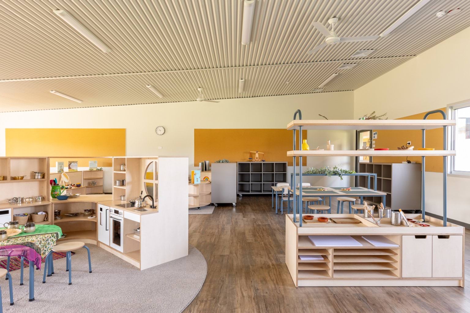 Learning space with a play kitchen, activity benches and open shelving arranged for early years education.