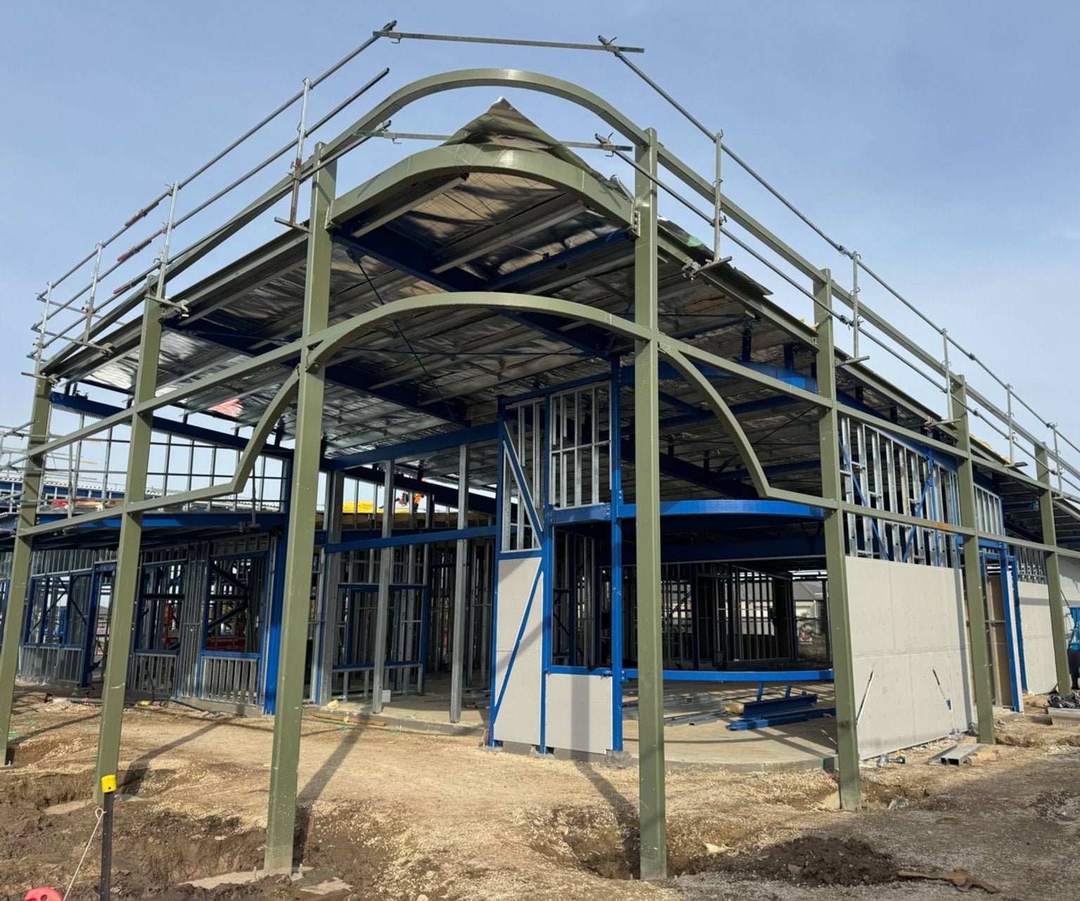 Two‑storey school building under construction with steel framing, curved beams and scaffolding in place.