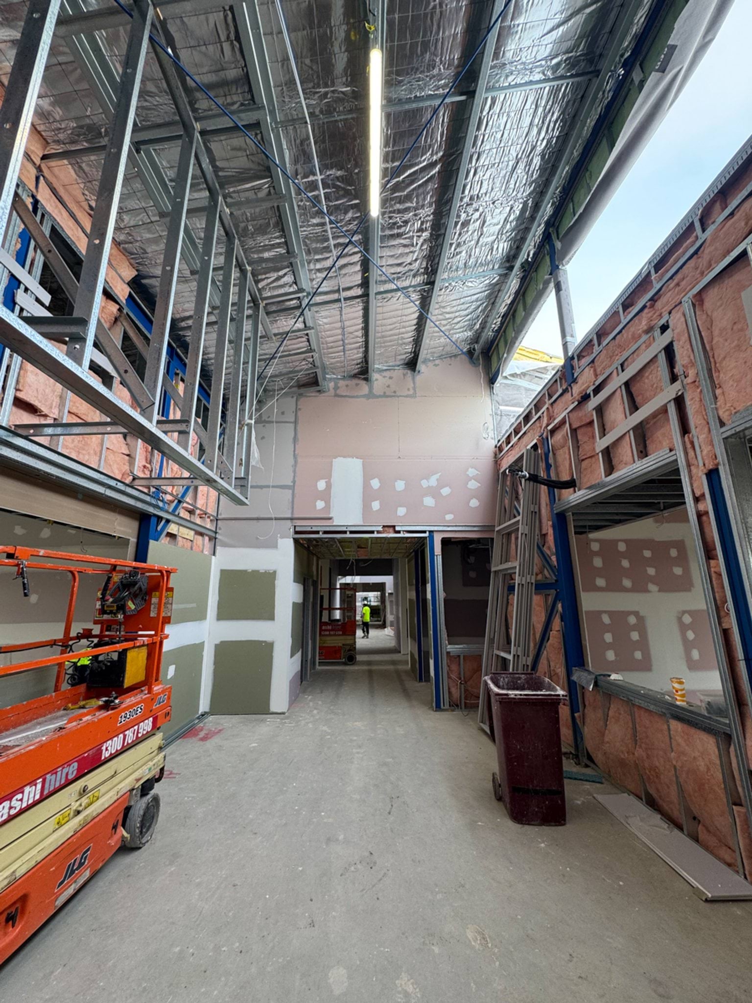 Partially completed school building with roof scaffolding, wrapped walls and construction materials on site.