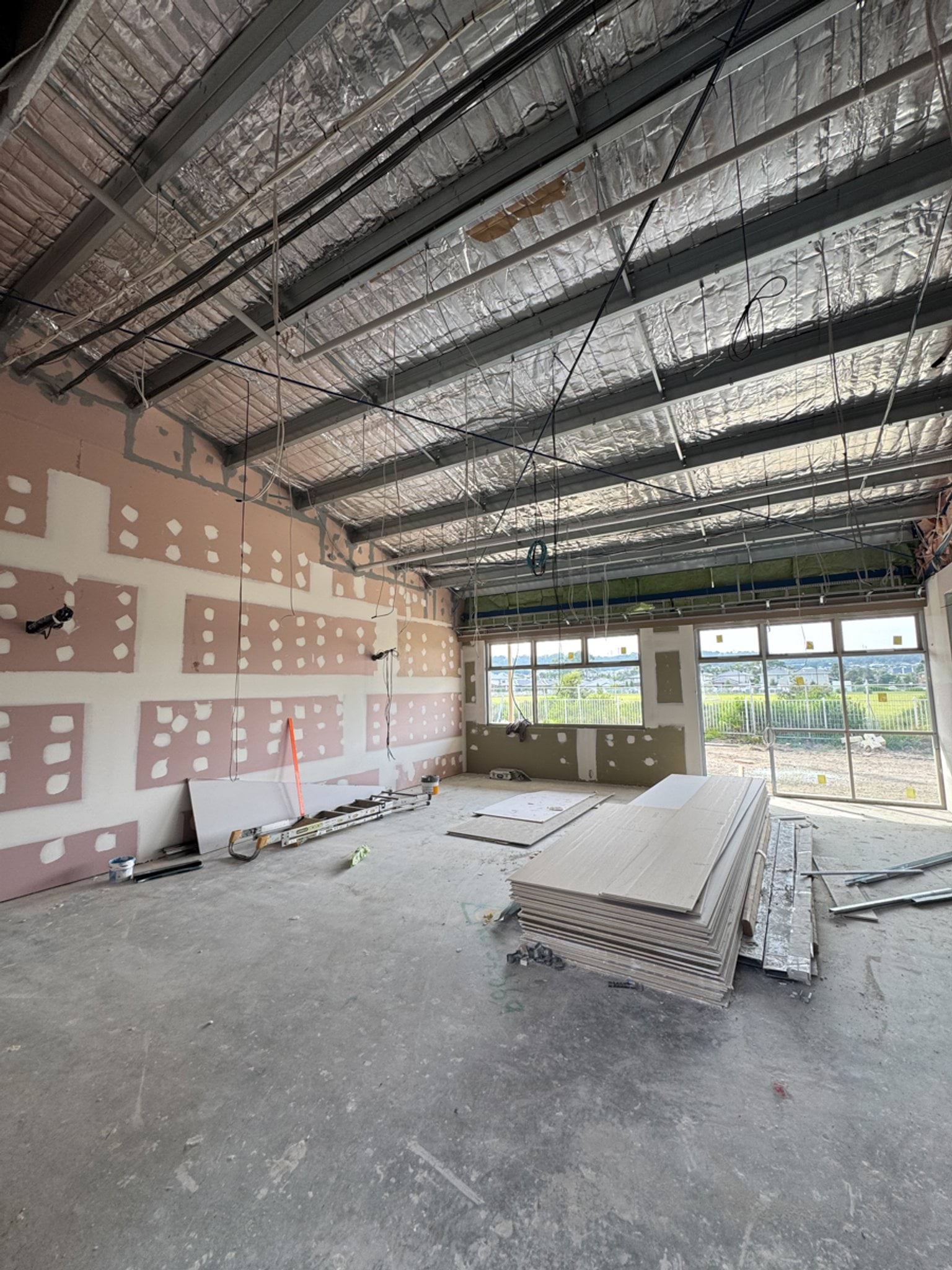 Interior of a school corridor under construction with wall framing, insulation and ceiling services exposed.