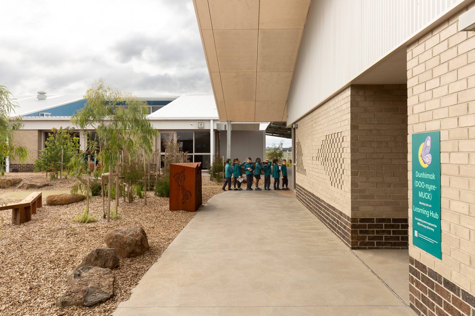 Students queuing outside building on footpath with garden
