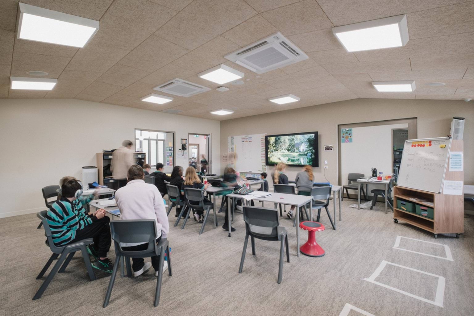 Carpeted classroom with screen and whiteboard. We can see students and teachers seated around desks