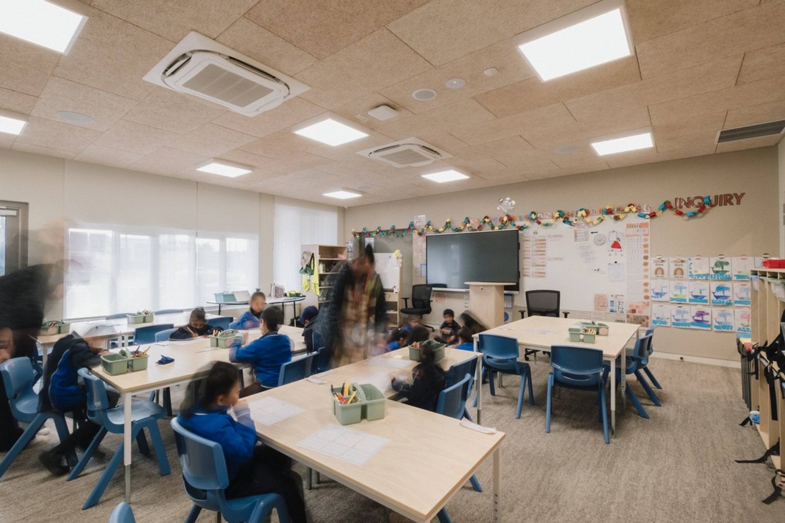 Classroom with grey patterned carpet, a screen and whiteboard and tables and chairs throughout