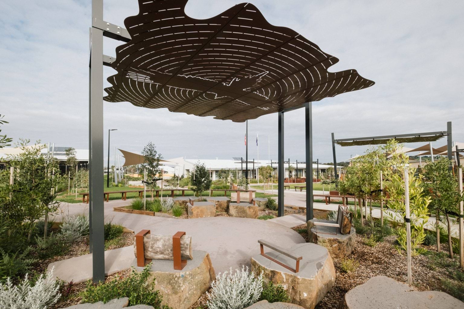 Outdoor garden area with paved walkways throughout and a large shelter with cut out first nations artwork