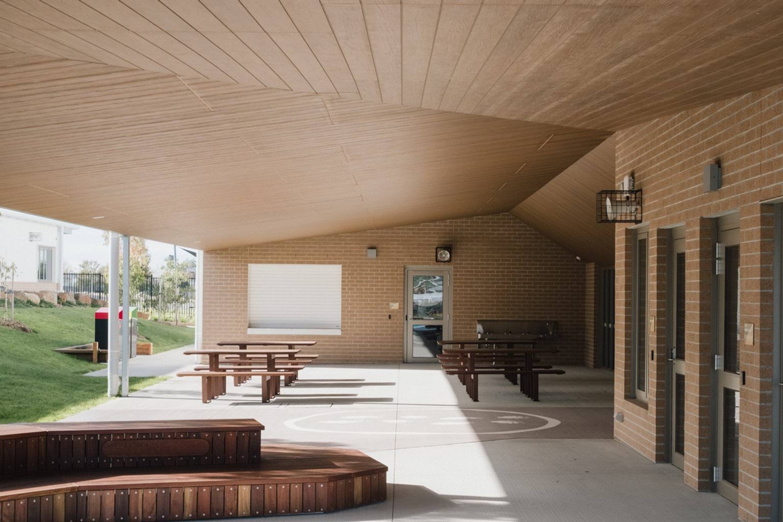 Covered outdoor area attached to building with paved area, wooden benches and wooden tables