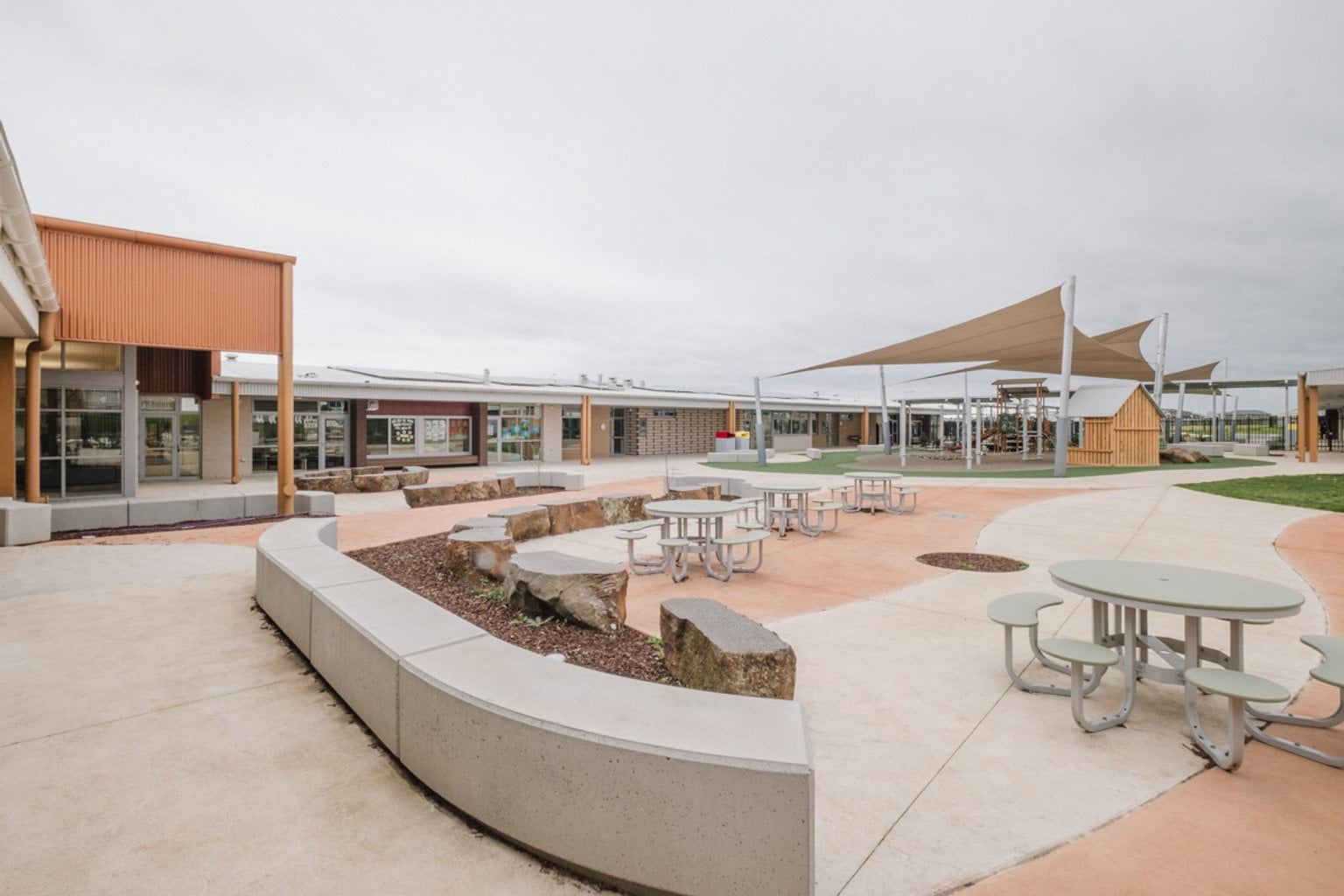 Outdoor paved area with tables and benches. We can see a covered play area in the rear of the space