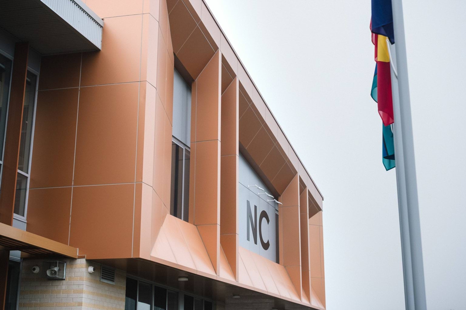 Orange building with large letters NC and a flag pole showing Indigenous and Torres Strait Islander flags