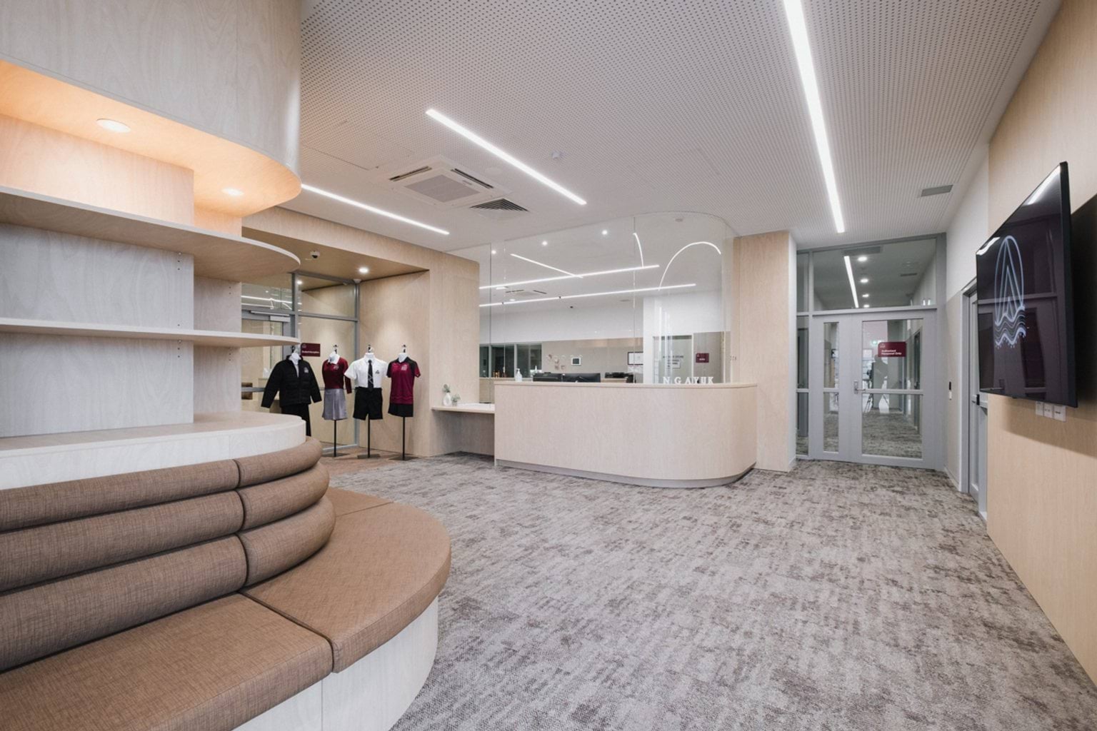 Carpeted reception area with curved, cushioned seating, a doorway and four mannequins displaying school uniforms