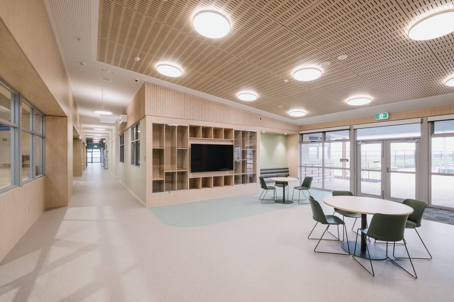 Open area with walkway, two circular tables with chairs, a large screen and shelves and a doorway and windows