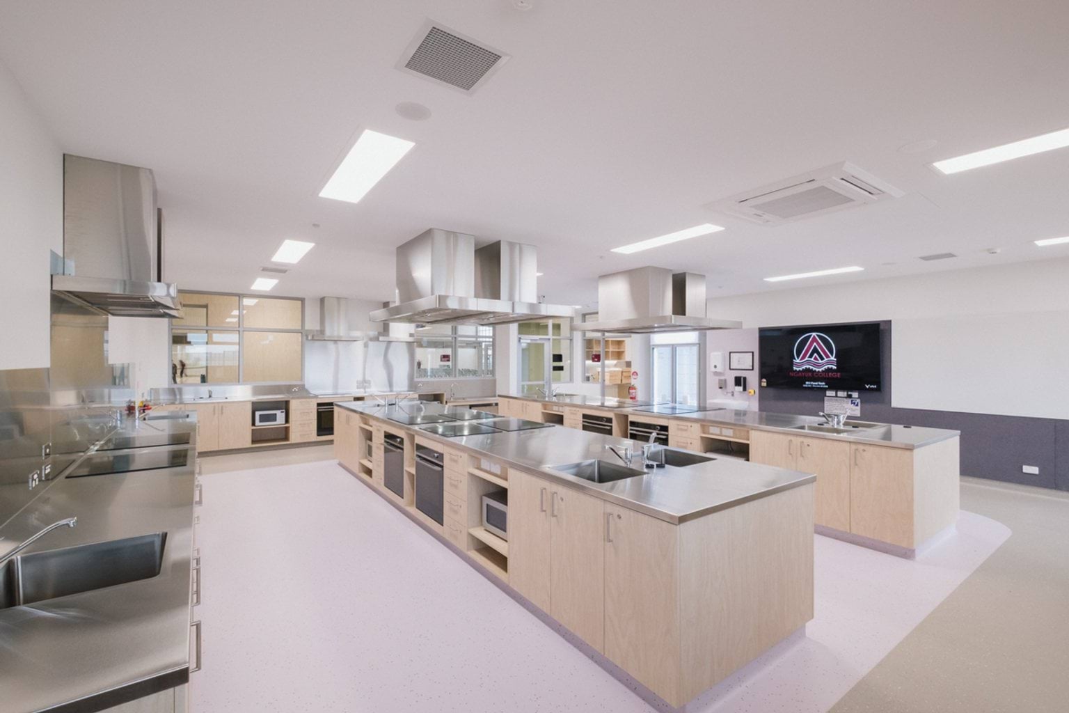 Food tech classroom with rows of metal counter tops each fitted with extraction fans, sinks, ovens, stoves and microwaves