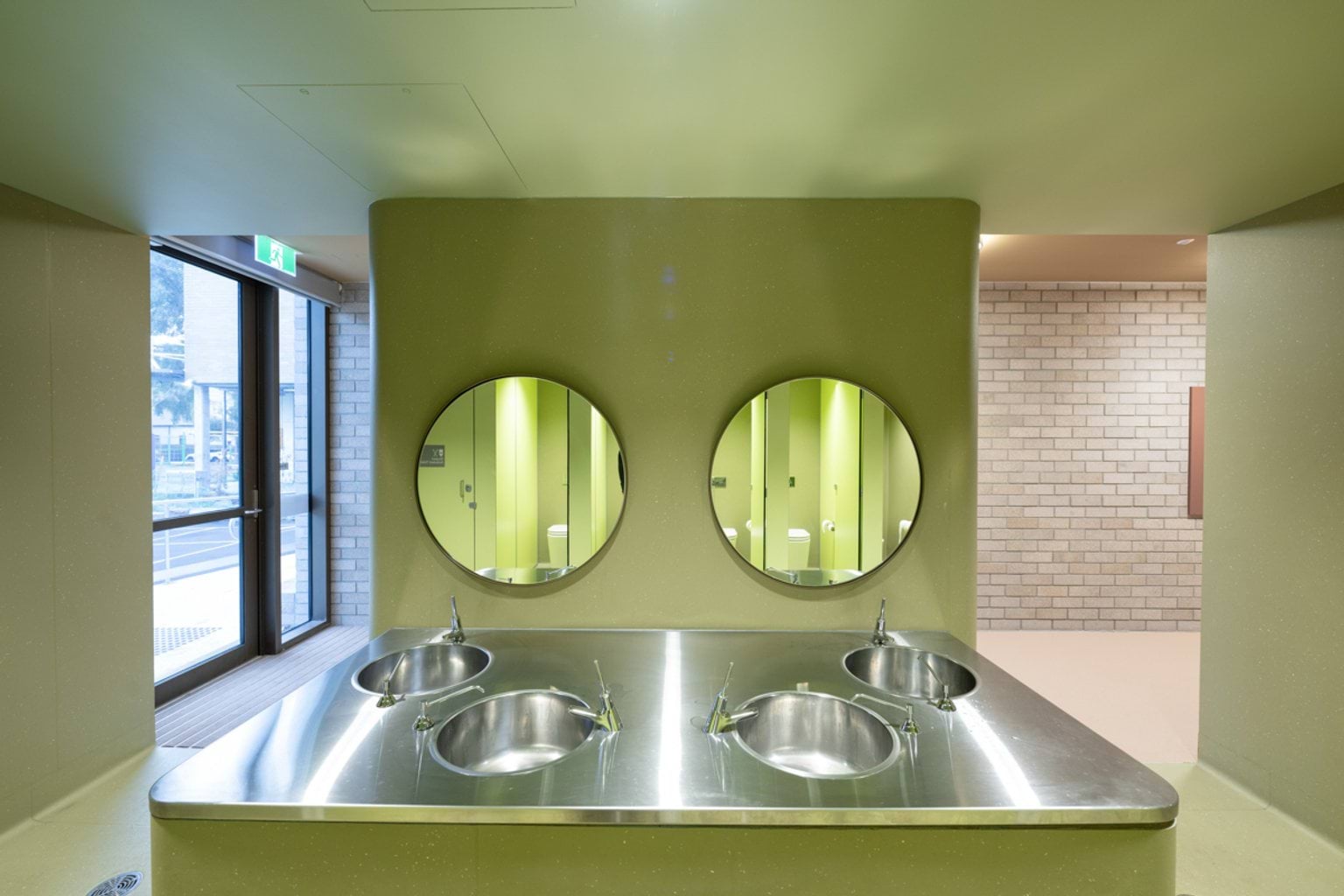 Light green open bathroom area with metal basins and benchtops and circular mirrors