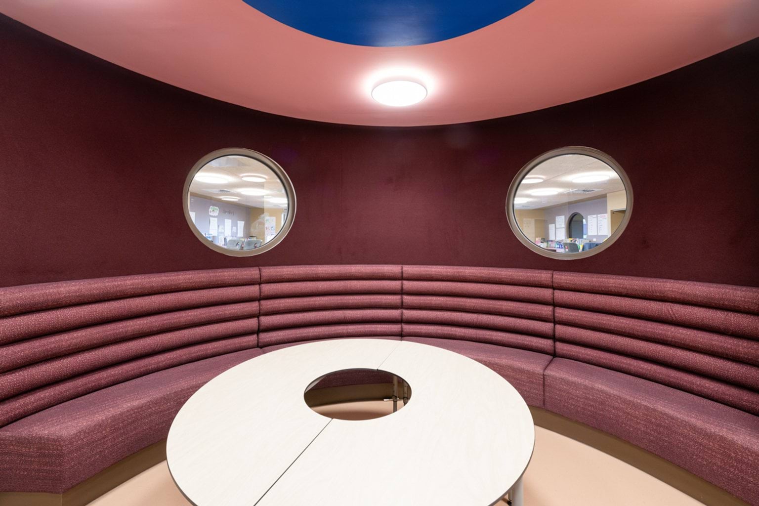 Mauve seating area with two circular windows and rounded mauve seating with a circular table