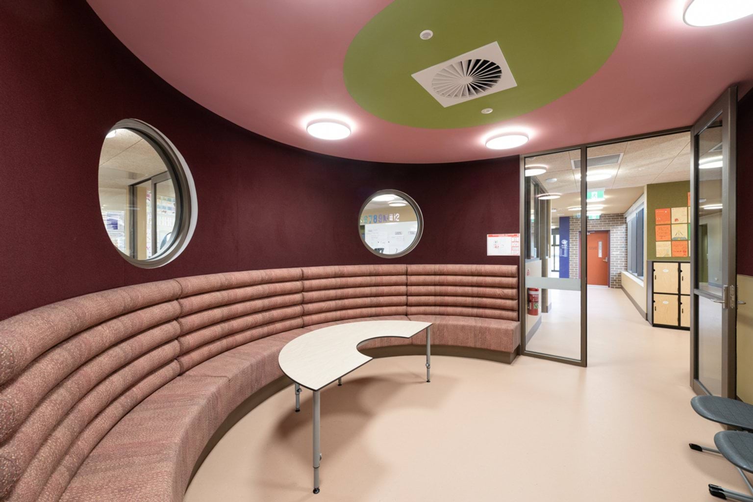 Curved mauve seated area with cushioned seats, curved table and circular windows
