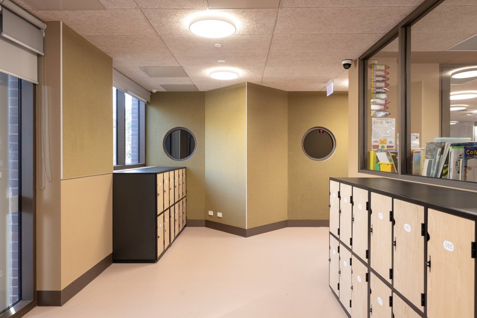 Hallway with lockers and a window which sees into a classroom on the right hand side.