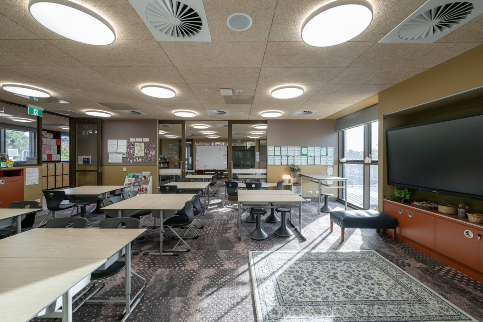Open plan classroom with sliding doors, grey patterned carpet, a screen with orange cabinets below and tables and chairs throughout