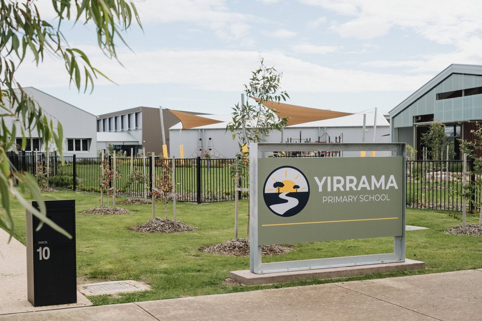 Street entrance of primary school with grass area in front of footpath and a sign with logo and 'Yirrama Primary School'