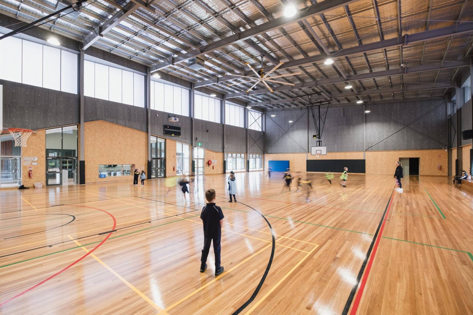 Indoor basketball stadium. We can see students running around on the court. 