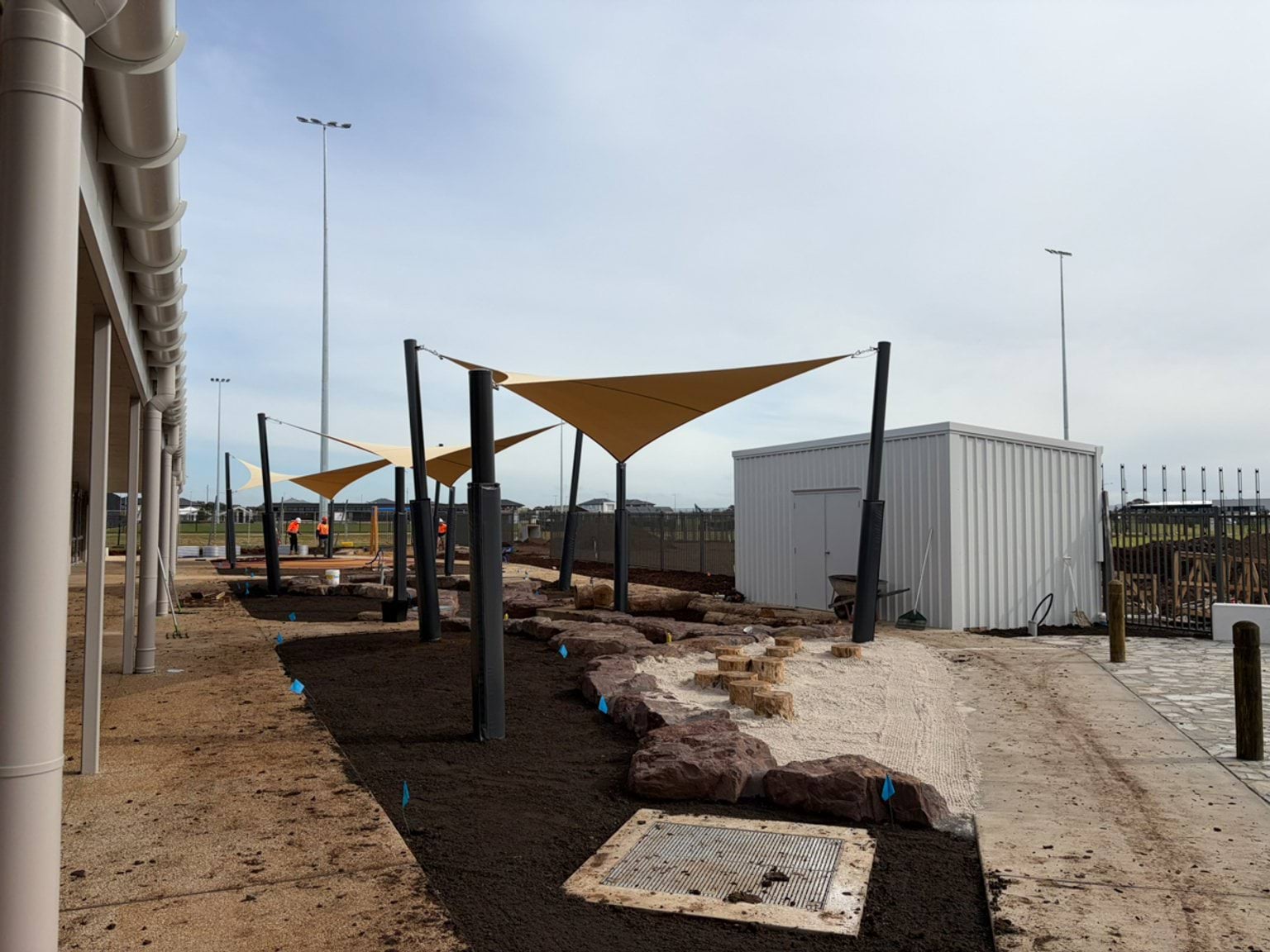 An outdoor service and landscaped area alongside a building, showing pathways, sandpits and garden beds.