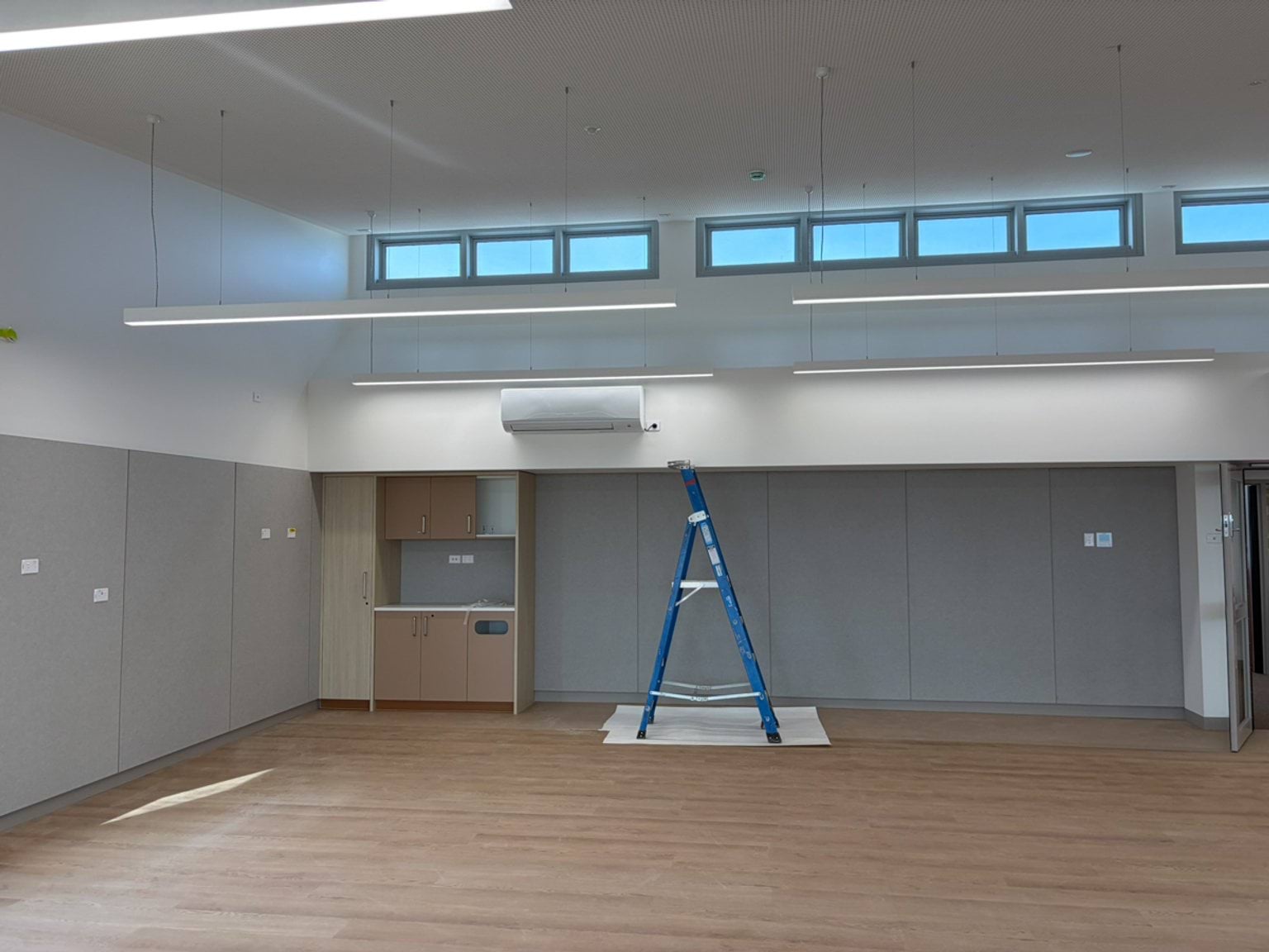 A near-completed room with timber flooring, high windows, grey walls and a ladder