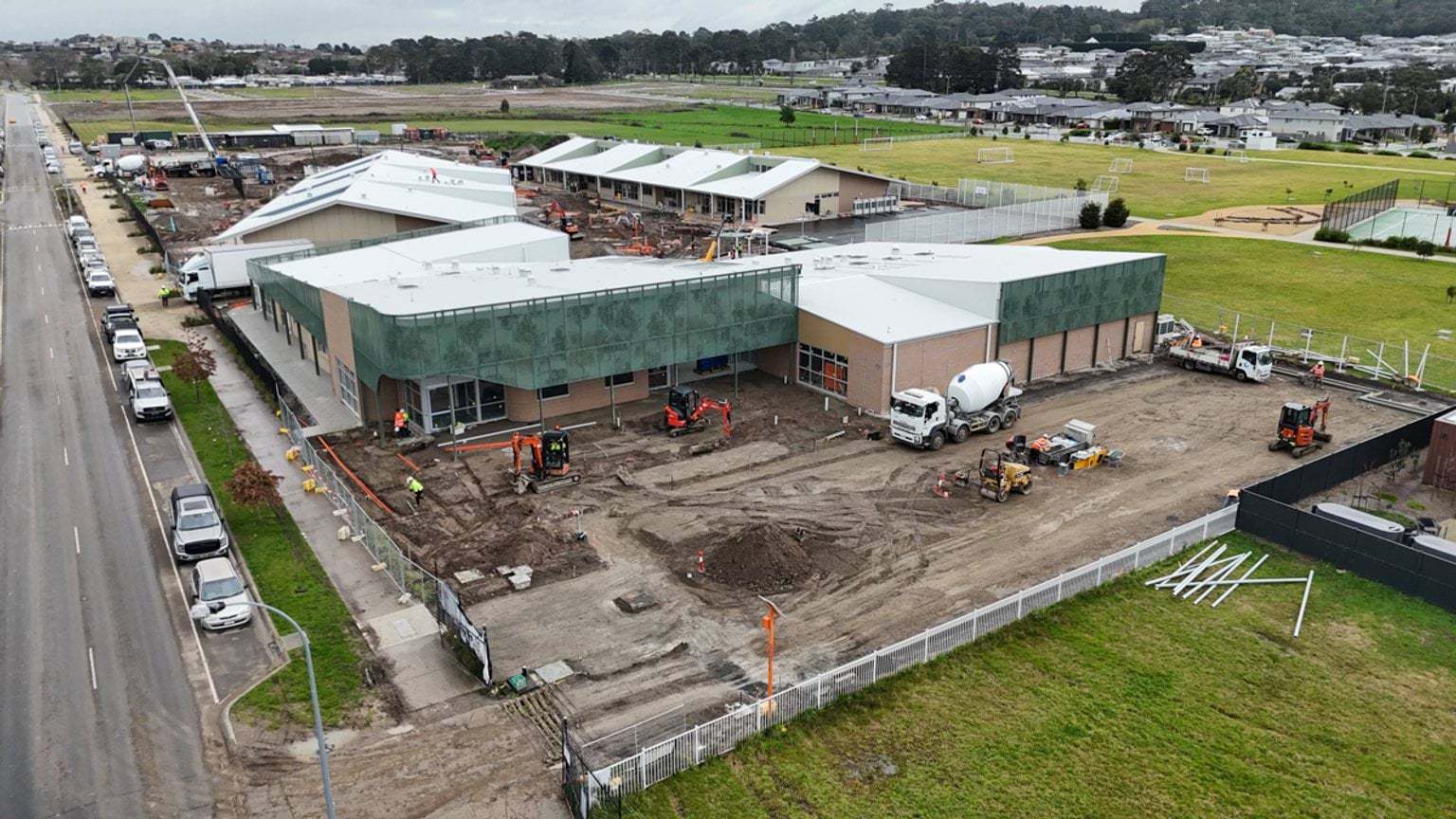 Aerial view of a large building under construction with large dirt work area within fenced site.