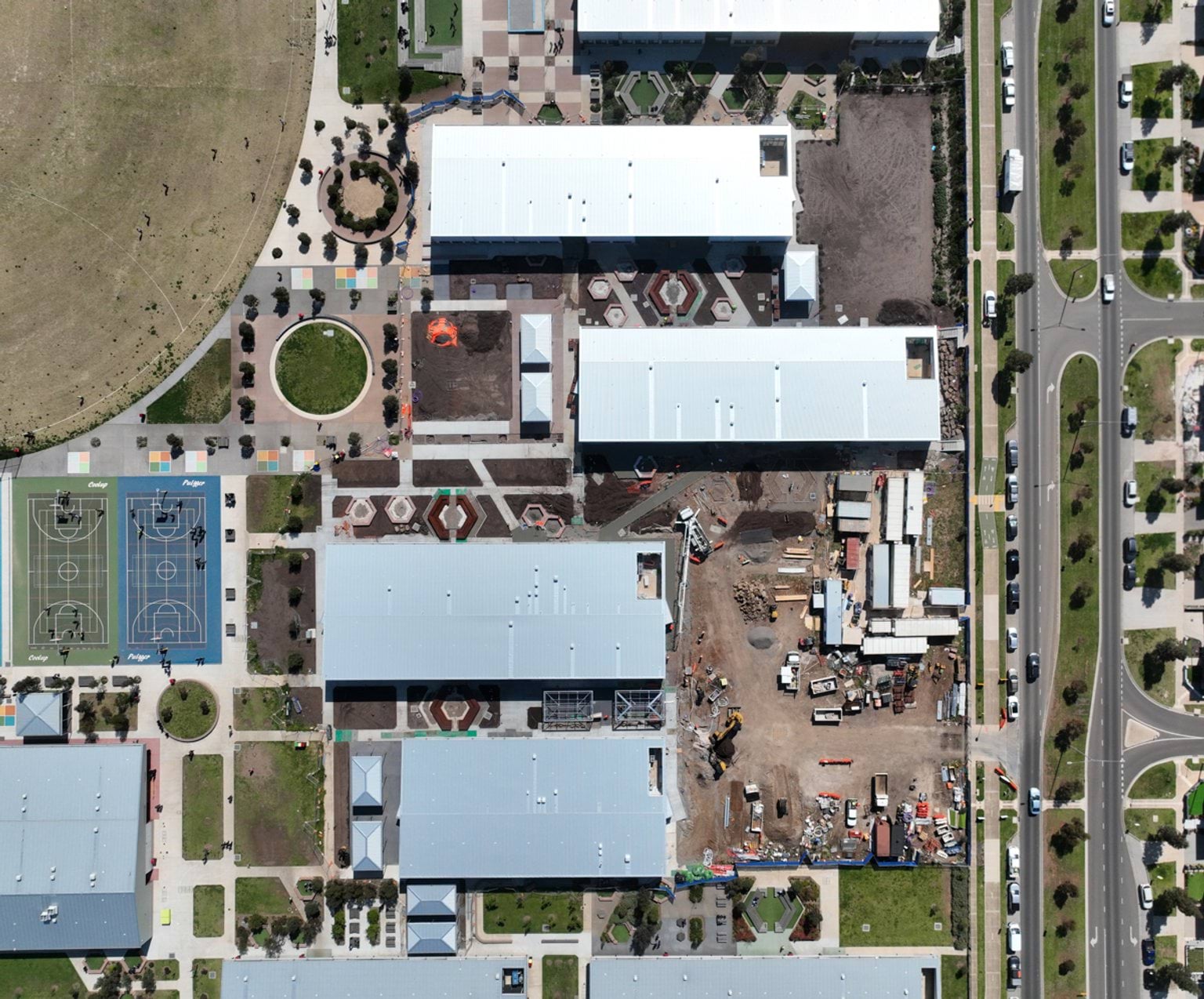 A bird’s-eye view of a school site showing several buildings, landscaped outdoor areas, sports courts and construction works in the centre of the campus.