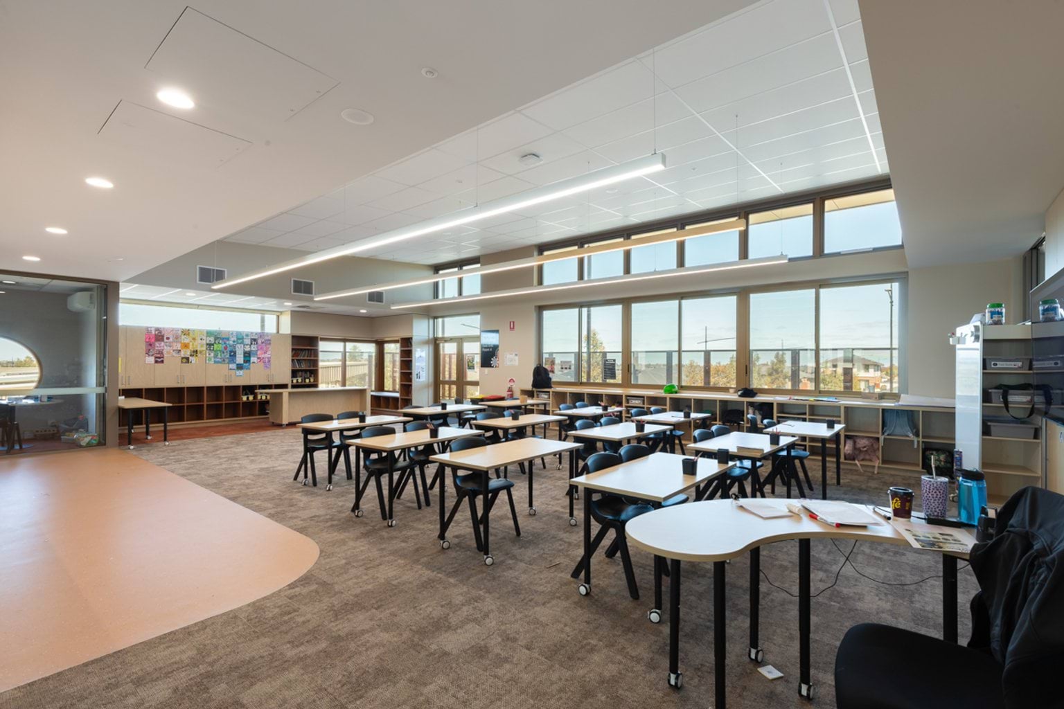Classroom with large windows along one wall, carpet throughout and rows of tables and chairs 