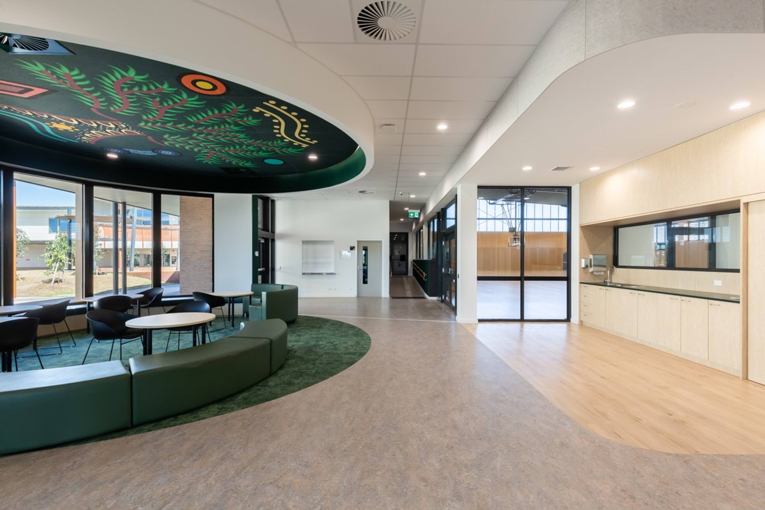Open foyer and a green, curved breakout area with bench seats and tables facing out to windows.