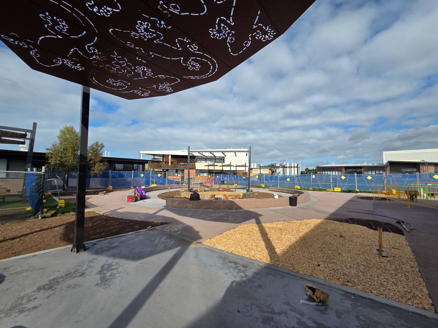 outdoor school or community space under construction, featuring curved pathways, landscaped garden beds, shade structures and a central gathering area.