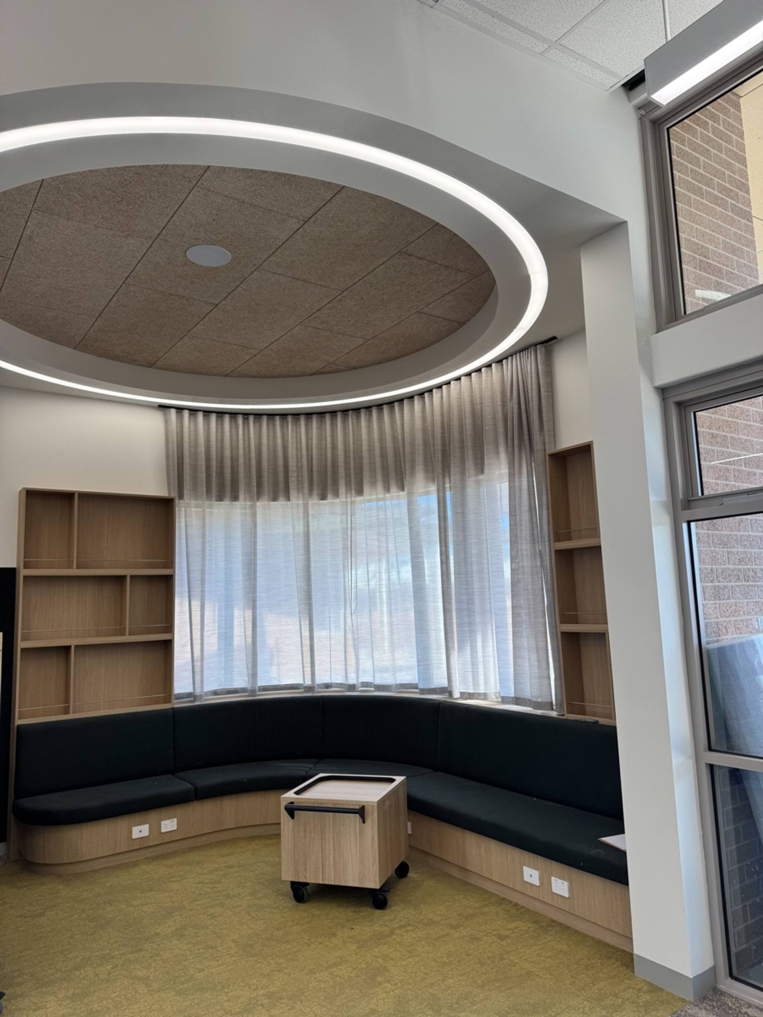 Indoor curved seated area with curved lighting, bookshelves and curtains covering a window